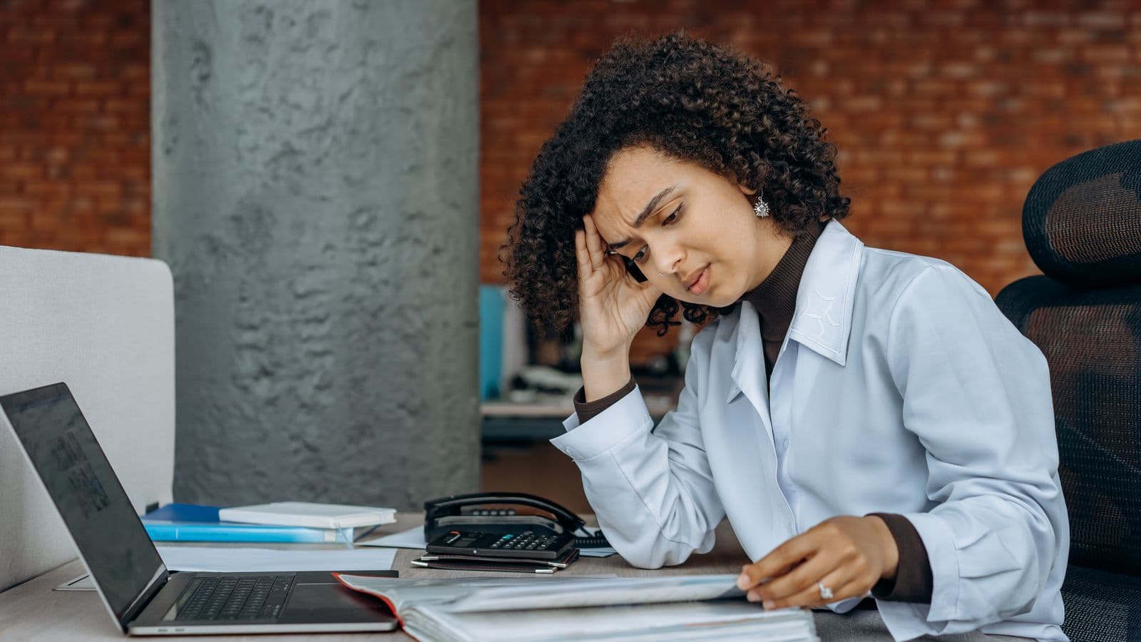 A businesswoman experiencing fatigue while working through financial paperwork and reconciliations at her desk