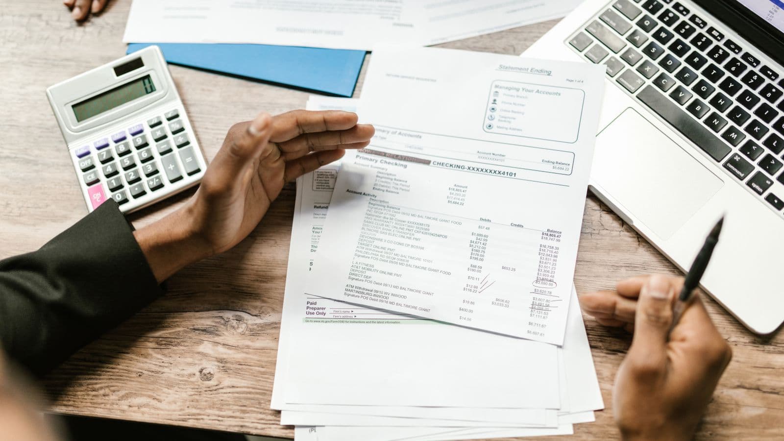 Hands holding financial documents with a calculator and laptop while reconciling accounts on an office desk